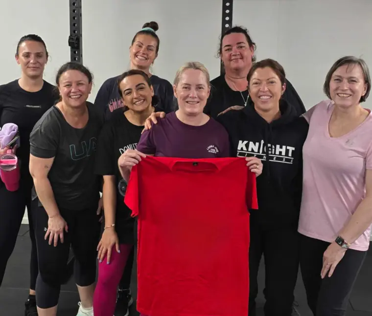 Women's Club members gathered around a member holding up a red Knight Fitness shirt