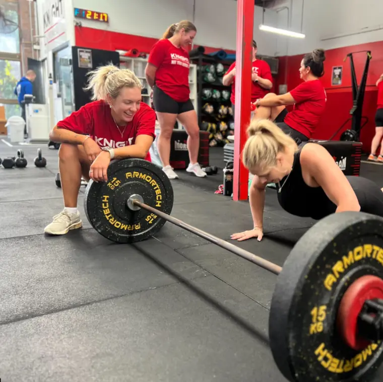 A Knight Fitness coach guiding members through a barbell session
