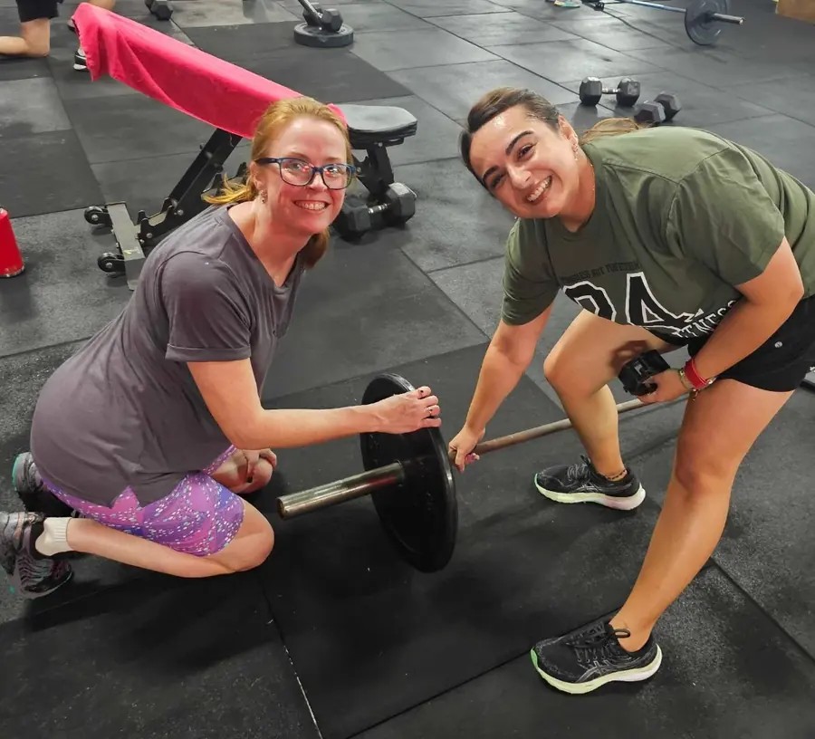 Two Women's Club members loading a barbell together during a coached session