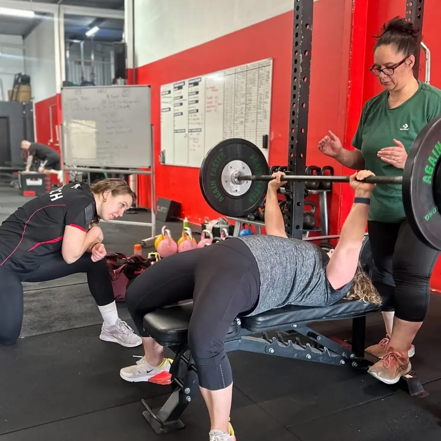 A Knight Fitness coach spotting a Women's Club member on the bench press